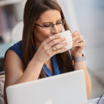 Carolyn Robistow headshot sitting at computer drinking coffee